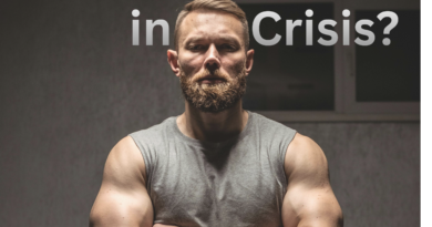A Man stands in a gray sleeveless shirt with his arms crossed looking sternly into the camera with the title caption, Masculinity in crisis?