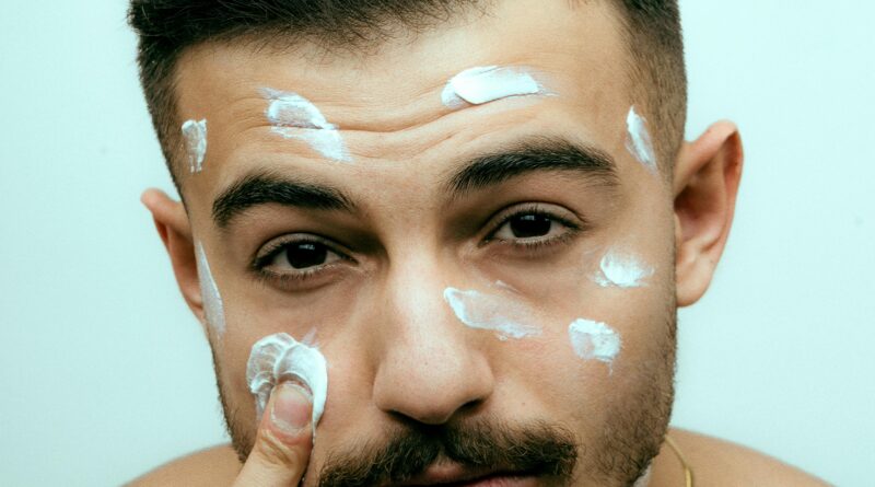 Close-up of a young man applying facial cream for skincare routine.