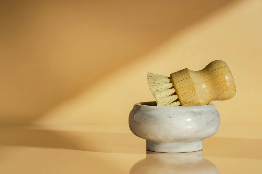 A bamboo cleaning brush in a marble bowl, minimalist and eco-friendly design captured on a beige background.